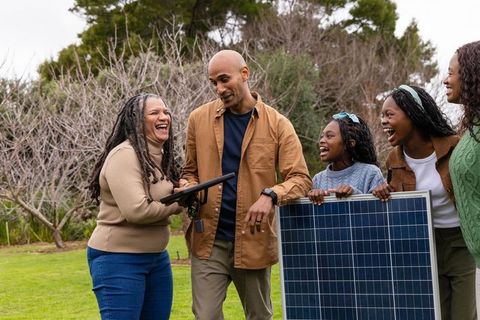 Laughing multigenerational group installing solar panel and checking tablet on lawn