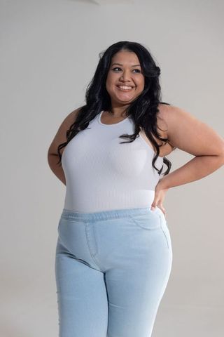 Smiling plus size woman posing in white ribbed tank and light blue high-waist jeans