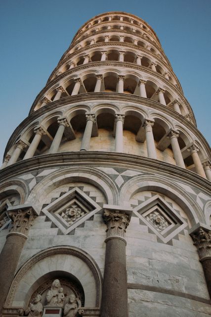 Close-up view of the Leaning Tower of Pisa at dusk, showcasing its intricate arches and columns. The famous structure, part of a historical attraction and UNESCO World Heritage site, is a significant architectural marvel. Ideal for use in travel guides, architecture studies, tourism advertisements, and cultural education material.