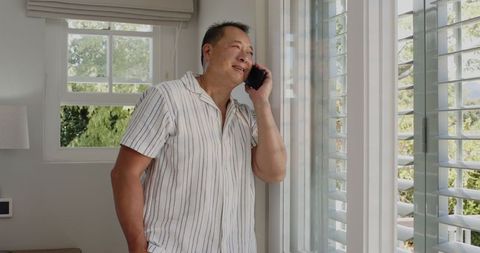 Senior man conversing on smartphone by window at home