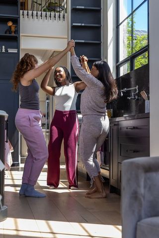 African american friends dancing together in sunlit modern kitchen holding hands laughing