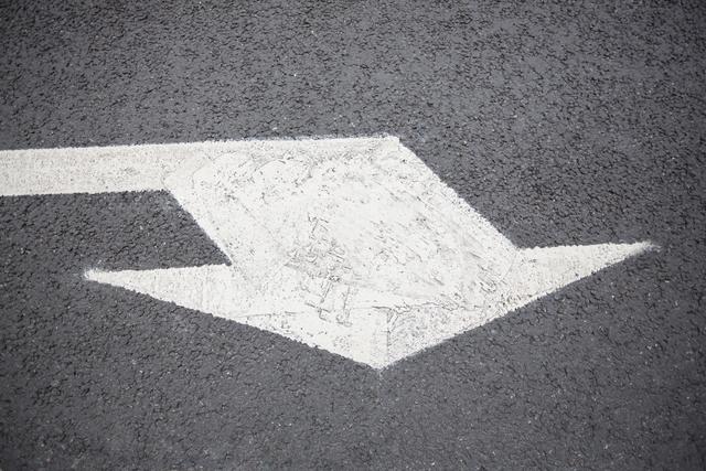 This image shows a directional arrow on an asphalt road surface. The arrow is painted clearly and represents direction for drivers to follow, making it useful for contexts related to navigation, traffic regulation, and transportation infrastructure. It can be used in traffic management publications, urban planning presentations, driving school materials, and apps related to maps and navigation.