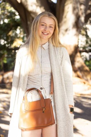 Smiling young woman wearing cardigan and smartwatch carrying leather handbag in sunlit park
