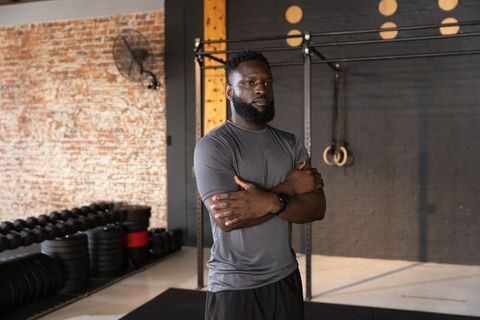 African american fitness coach standing arms crossed in crossfit gym with rings and dumbbells