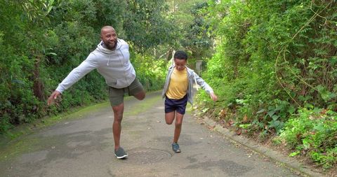 African american father and son balancing on one leg on leafy lane, playful family bonding