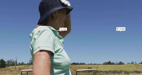 Senior woman scanning golf fairway wearing sun hat and polo with digital ui location tags