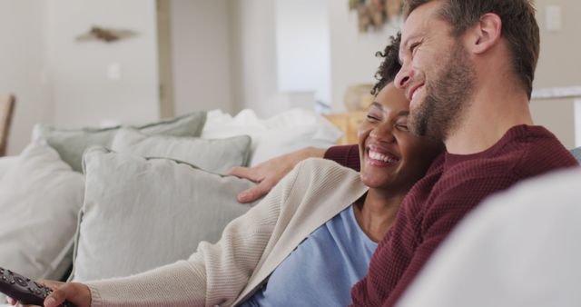 Image of happy diverse couple watching tv on sofa. Love, relationship and spending quality time together at home.