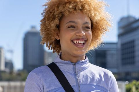 Joyful african american woman smiling in urban athleisure jacket, city lifestyle portrait