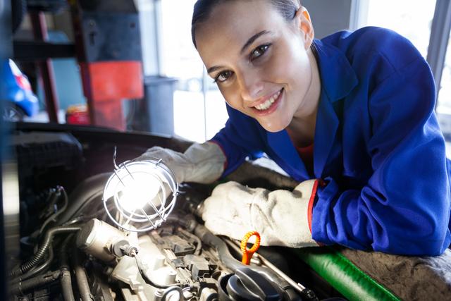 Portrait of female mechanic examining car engine at the repair garage