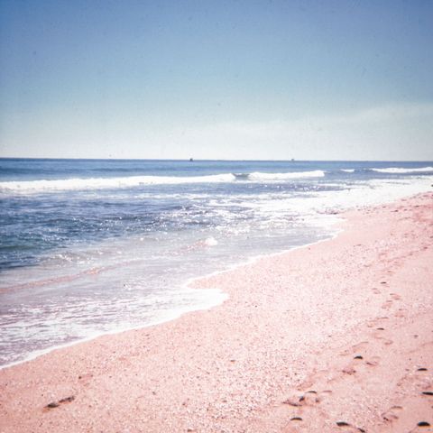 Sunlit pastel beach shoreline with gentle waves rolling and footprints tracing sand