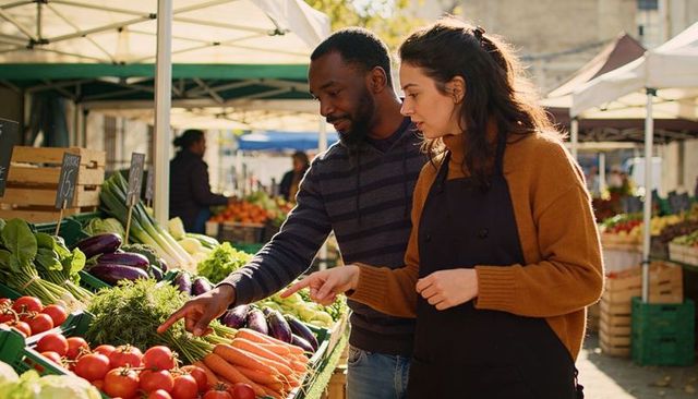 Vendor and customer selecting fresh produce at sunny farmers market stall