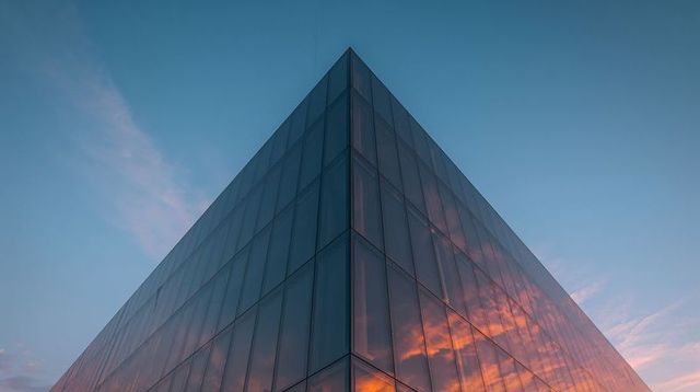 Glass apex reflecting vibrant sunset clouds on geometric facade