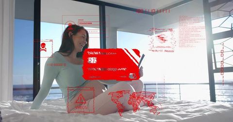 Woman sitting on bed holding tablet with red cybersecurity holographic interface by ocean