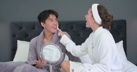 Diverse couple sharing skincare routine woman applying facial device man holding mirror