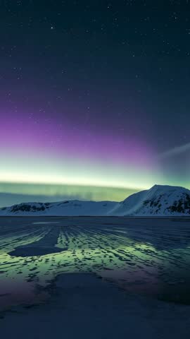 Vertical aurora borealis painting sky and reflecting on frozen Arctic shoreline
