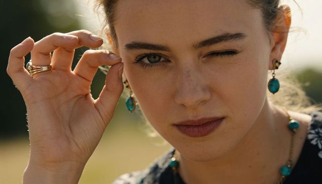 Winking woman touching earlobe at golden hour with turquoise earrings and sunlit freckles