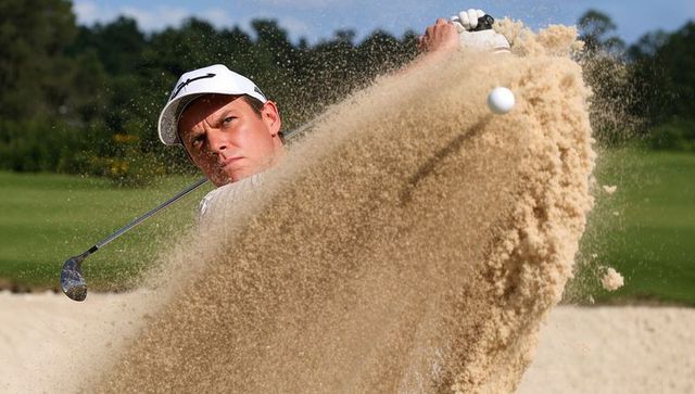 Golfer hitting explosive bunker shot sending sand plume and ball midair wedge precision action