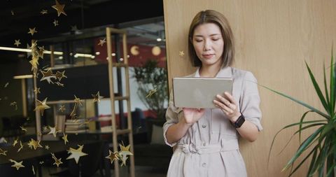 Leaning asian woman checking tablet in modern coworking space with wood panel and greenery