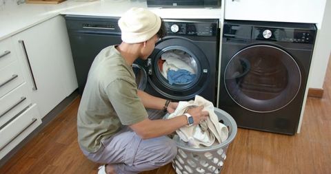 Young african american man loading front-loading washer in modern home laundry nook