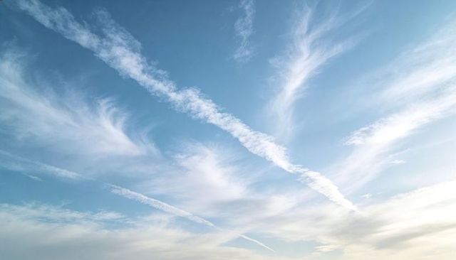 Drifting cirrus clouds and crossing jet contrails over pale blue sky at horizon