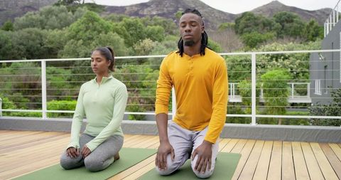 African american man and indian woman meditating on rooftop deck for mindfulness practice