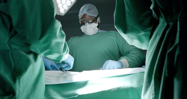 Focused diverse surgeons wearing face masks during surgery in operating room. Medicine, healthcare and hospital, unaltered.