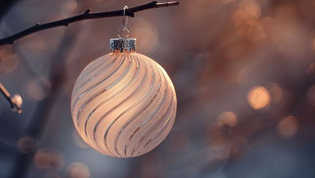 Hanging champagne christmas bauble glowing with spiral glitter and warm bokeh dusk