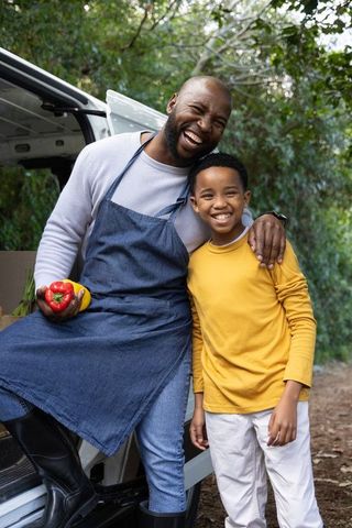 African american father and son selling fresh peppers from market van, smiling together