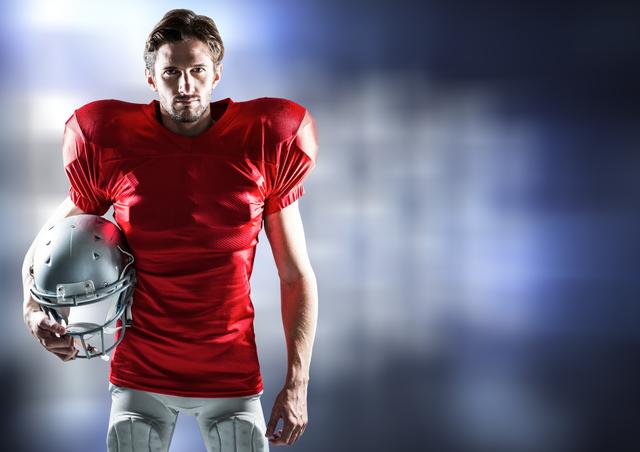 This dynamic image shows a confident American football player wearing a red jersey and holding a helmet against a blurred background. It is ideal for use in sports-themed articles, motivational content related to athletic performance, promotional materials for football events, and advertisements for sports equipment.