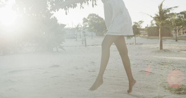 Woman strolling barefoot on a beach during sunset, dressed in a white dress. Perfect for use in travel brochures, relaxation, summer vacation themes, lifestyle blogs, advertisements promoting tranquil coastal getaways, and nature-related content.