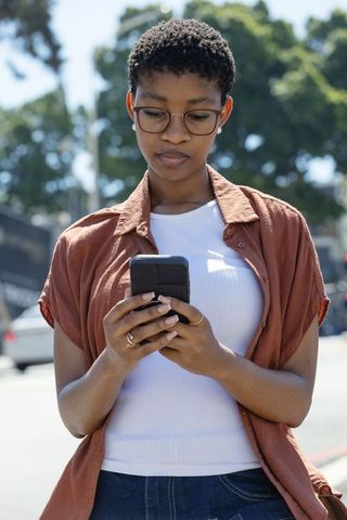 African american woman standing and looking at smartphone, wearing glasses and casual denim