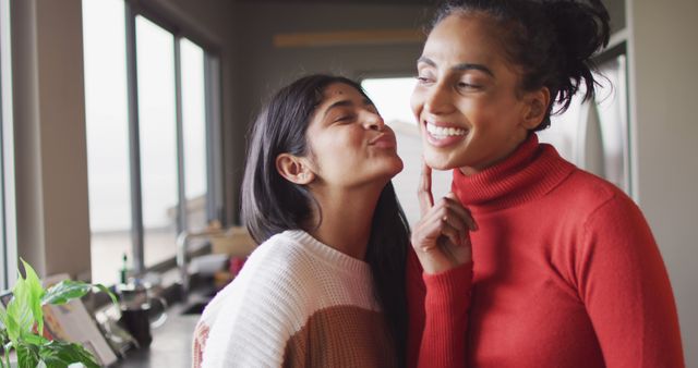 Image of happy biracial female friends kissing on cheek. Friendship, having fun and spending quality time together at home.