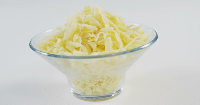 A glass bowl filled with shredded cheese sits against a white background, with copy space. Ideal for culinary themes, the image showcases a common ingredient used in various recipes for added flavor and texture.