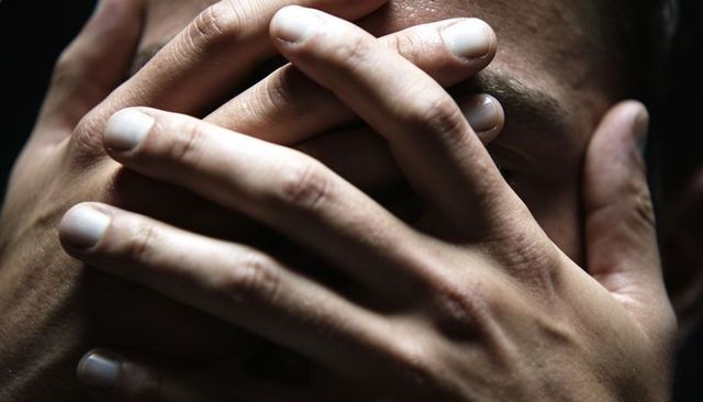 Close-up male hands covering face interlaced fingers conveying anxiety and concealment