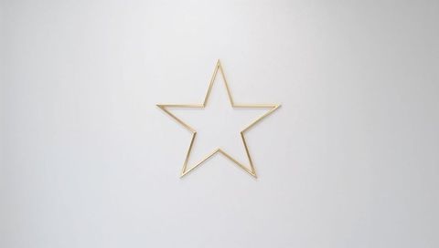 Hanging gold metal five-point star outline on smooth light gray wall with soft shadow