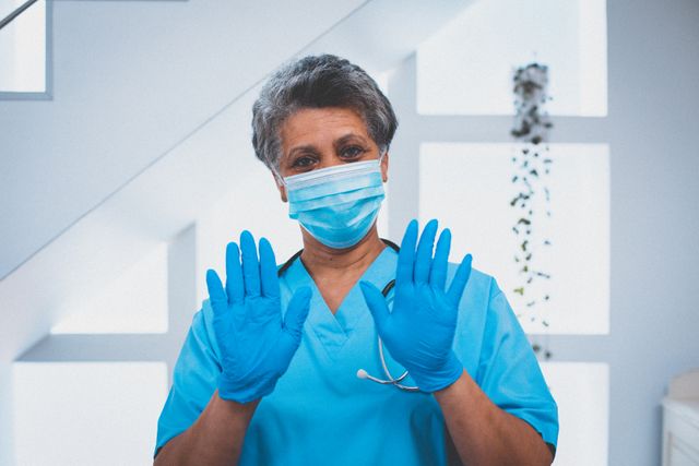 Portrait of african american female senior doctor in face mask and surgical gloves looking to camera. medical professional worker during coronavirus covid 19 pandemic.