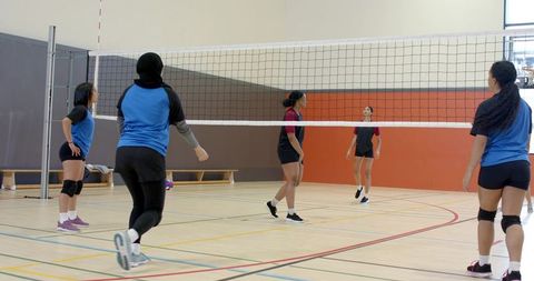 Diverse women playing indoor volleyball practicing net rotation and team positioning
