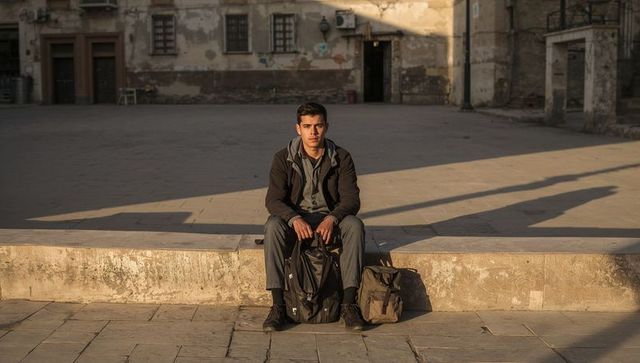 Young traveler sitting on sunlit urban curb holding backpack during golden hour