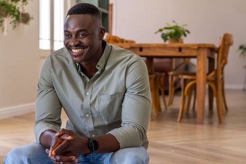 African american man smiling and sitting in cozy modern dining room casual lifestyle portrait