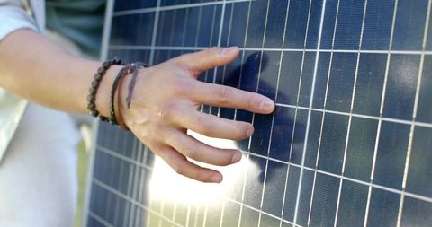 Male technician inspecting solar panel cells with hand and bracelets closeup in sunlight