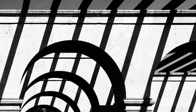 Monochrome arched arcade with dramatic slatted shadow bands minimalist study