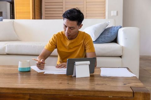 Asian Man Working from Home with Tablet and Papers, Studying and Managing Personal Finances