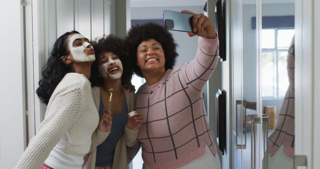 Happy diverse female friends taking selfies with smartphone and smiling in bathroom. spending quality time at home.