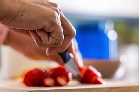 Mature woman slicing strawberries with paring knife on wooden cutting board