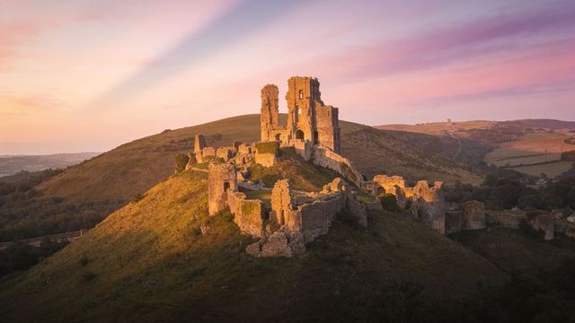 Ancient castle ruins basking in golden sunrise on rolling hilltop overlooking rural valley