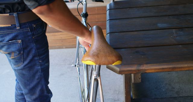 A person parks a bicycle next to a wooden bench, creating a casual and urban street scene. This image can be used for themes involving cycling, urban lifestyles, outdoor activities, or sustainable transportation. Suitable for use in advertisements, blogs, websites, and articles related to bicycling, street photography, or city living.