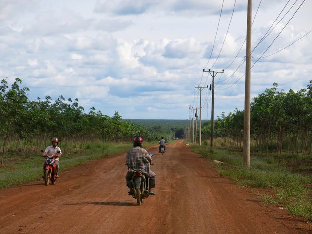 Motorcyclists exploring a dirt road in a picturesque rural area at sunset. Tall electricity poles line the route, adding to the scenic landscape filled with greenery under a blue sky with clouds. Perfect for travel blogs, adventure websites, and promotional materials showcasing rural tourism, off-road biking experiences, and the beauty of remote outdoor scenery.