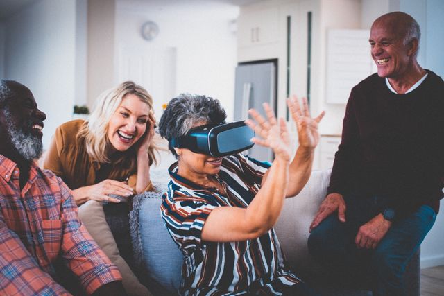 Diverse group of senior friends having fun at home watching female friend wearing vr headset. retirement lifestyle, socialising with friends at home.