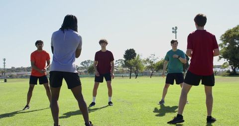 Diverse male team practicing coach-led drill for agility and footwork training outdoors