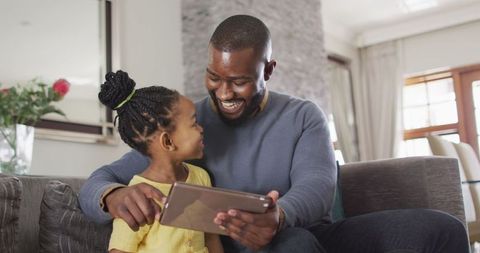 Happy Father and Daughter Bonding with Tablet on Sofa at Home